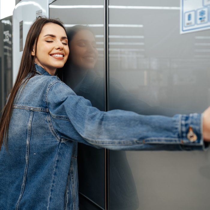 young happy woman leaning on her new refrigerator in a mall